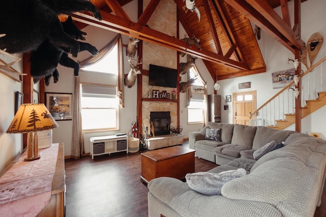 living area with plenty of natural light, beamed ceiling, a stone fireplace, and dark wood-type flooring