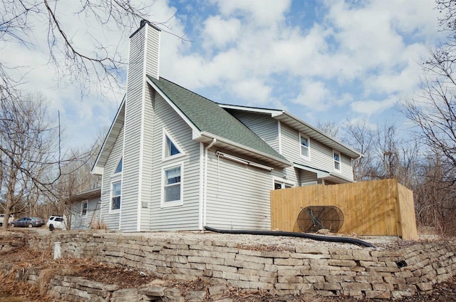 view of side of property with a shingled roof, a chimney, and fence