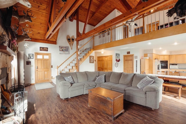 living area with beamed ceiling, stairway, a stone fireplace, wooden ceiling, and dark wood-style flooring