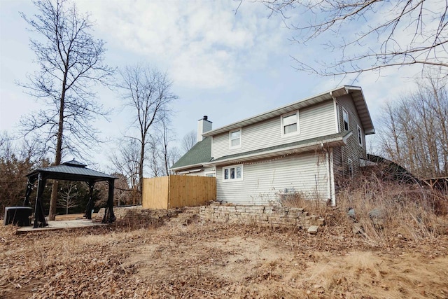 back of house with a gazebo, a chimney, and fence