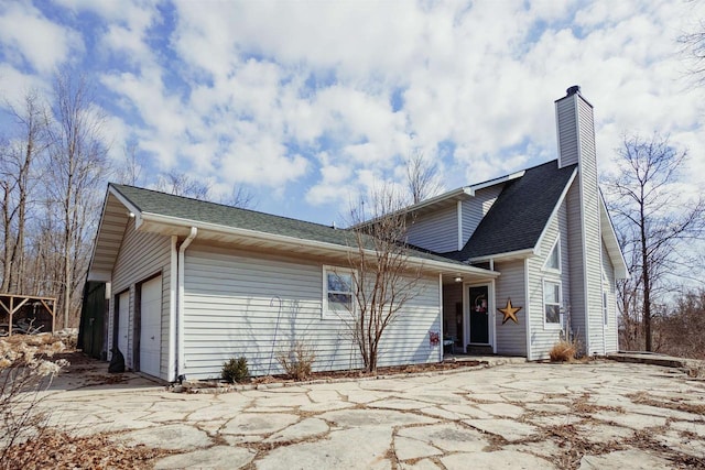 exterior space featuring an attached garage, a chimney, and roof with shingles