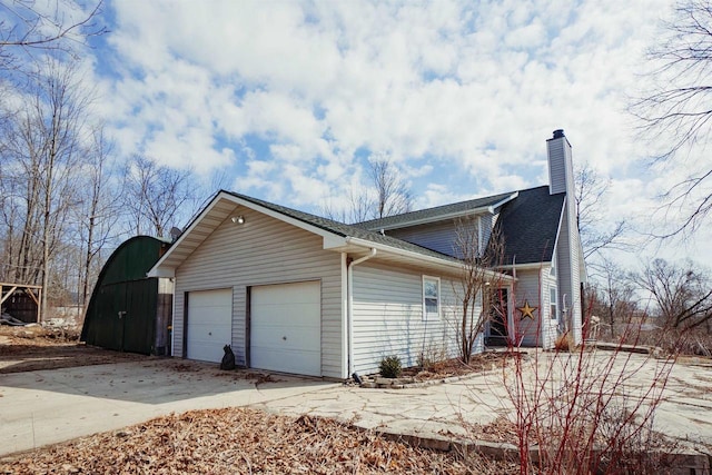 view of side of property featuring concrete driveway, a chimney, a garage, and roof with shingles