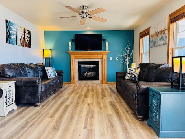 living area with a fireplace, a ceiling fan, baseboards, and light wood finished floors