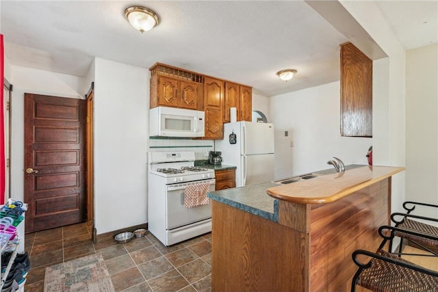 kitchen featuring white appliances, a peninsula, a sink, decorative backsplash, and brown cabinets