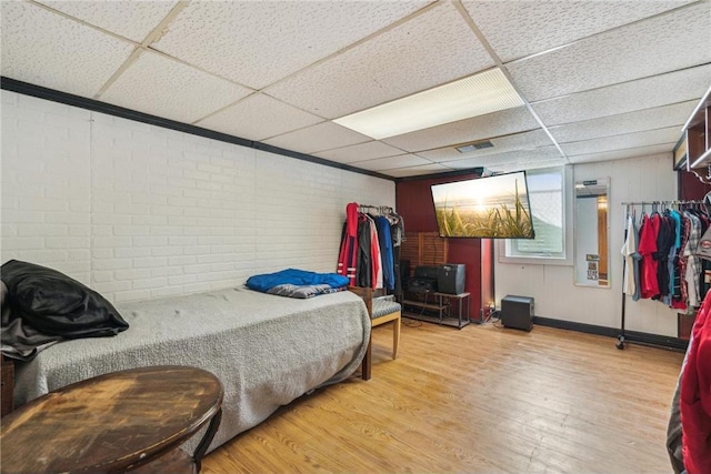 bedroom with visible vents, brick wall, light wood-type flooring, and a paneled ceiling