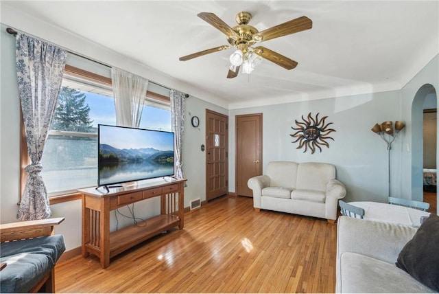 living room featuring arched walkways, visible vents, light wood finished floors, and a ceiling fan