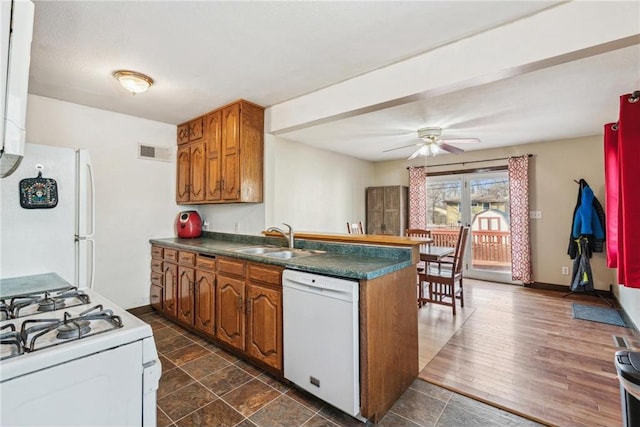 kitchen featuring white appliances, dark countertops, a peninsula, and a sink