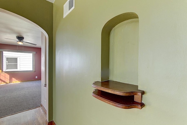 hallway with visible vents, arched walkways, and wood finished floors