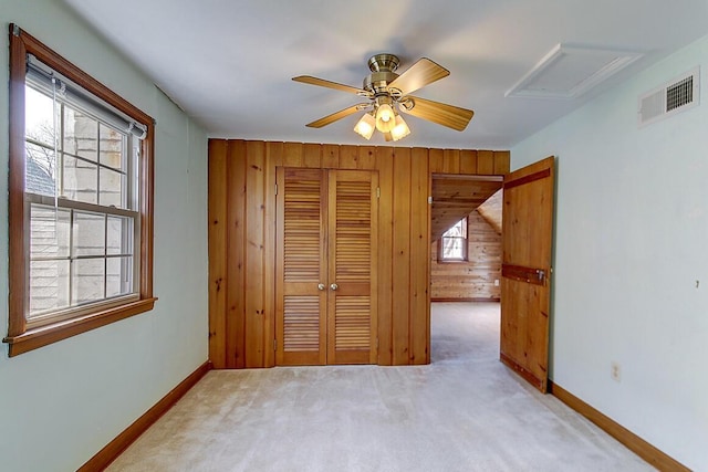 unfurnished bedroom with visible vents, a closet, wood walls, baseboards, and light colored carpet