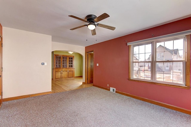 unfurnished room featuring carpet flooring, arched walkways, visible vents, and baseboards