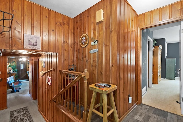 hall featuring an upstairs landing, wooden walls, and carpet