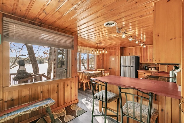 kitchen with visible vents, wood walls, wood ceiling, freestanding refrigerator, and wood finished floors