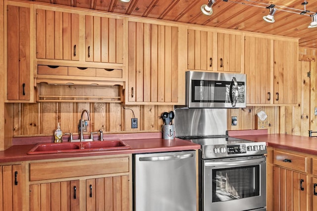 kitchen featuring wooden walls, light brown cabinetry, wood ceiling, appliances with stainless steel finishes, and a sink