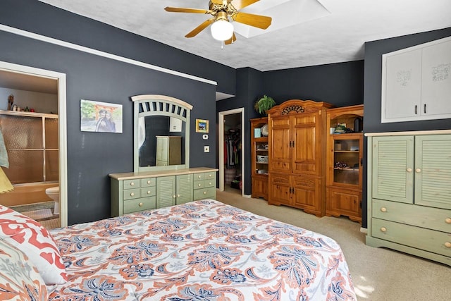 bedroom with a textured ceiling, ensuite bath, light colored carpet, and ceiling fan