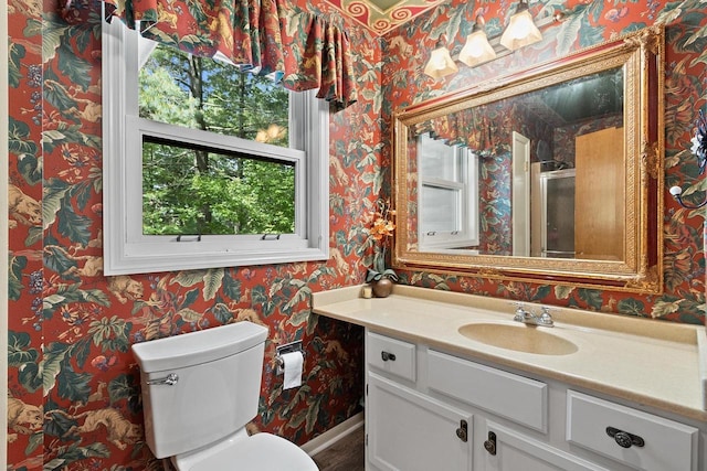 bathroom featuring wallpapered walls, baseboards, toilet, an enclosed shower, and vanity