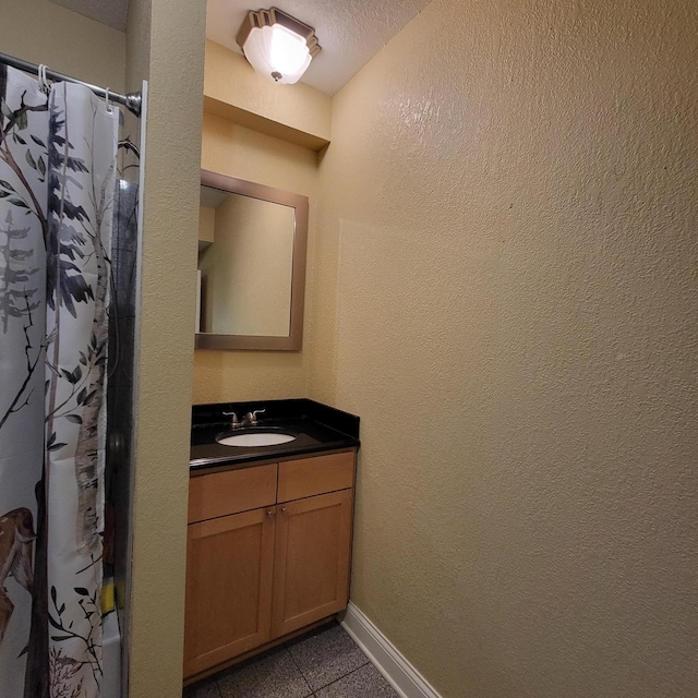 full bathroom with vanity, baseboards, a textured ceiling, curtained shower, and a textured wall