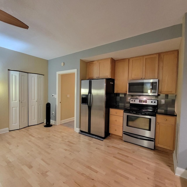 kitchen featuring light brown cabinetry, dark countertops, appliances with stainless steel finishes, and light wood-type flooring