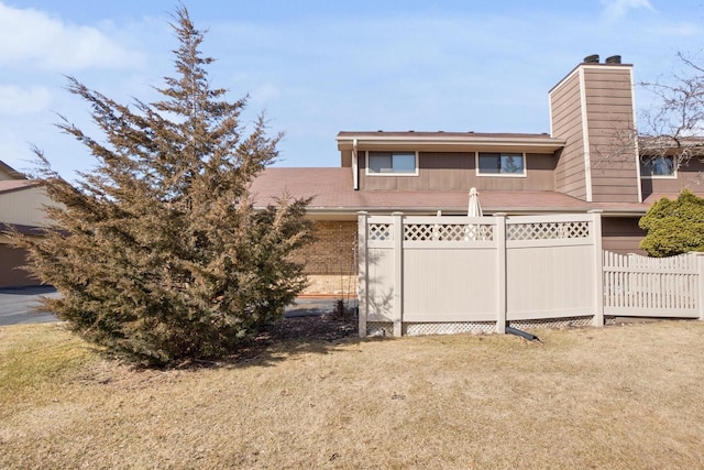 back of property with brick siding, a chimney, a yard, and fence