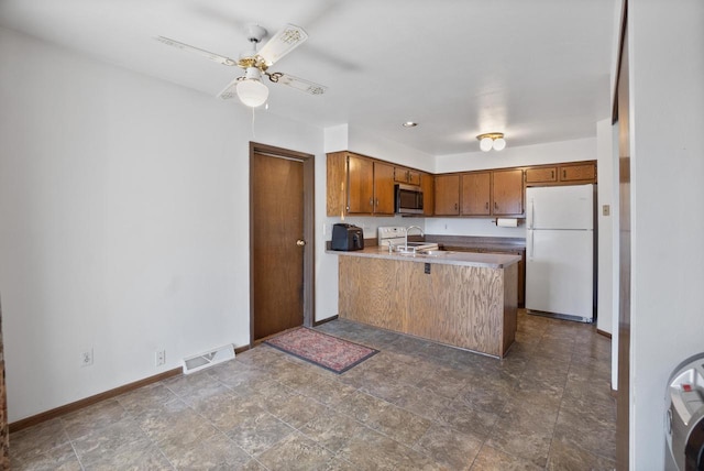 kitchen featuring visible vents, a peninsula, freestanding refrigerator, a sink, and stainless steel microwave