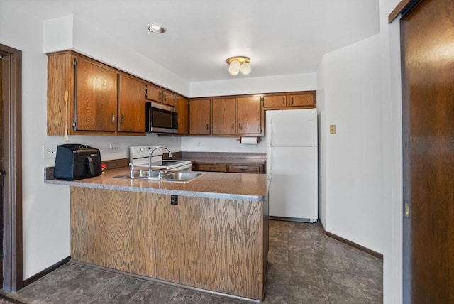 kitchen featuring baseboards, a peninsula, brown cabinetry, white appliances, and a sink