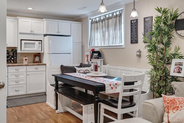 kitchen with white microwave, light wood finished floors, white cabinetry, and ornamental molding