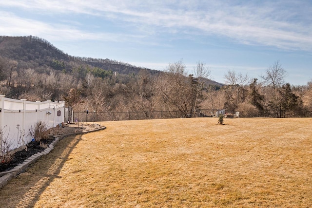 view of yard featuring a forest view, a mountain view, and fence