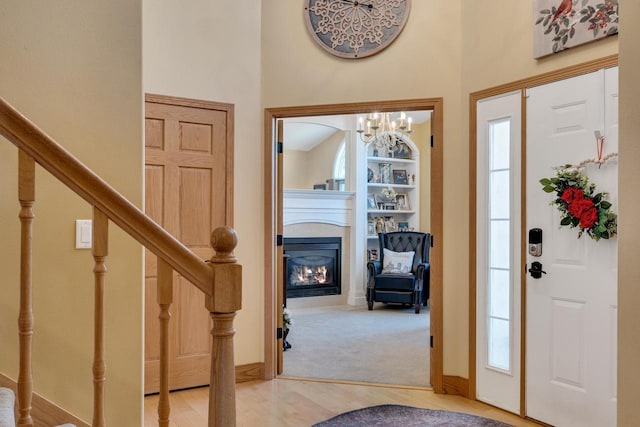 foyer with a glass covered fireplace, wood finished floors, baseboards, a towering ceiling, and stairs