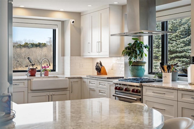 kitchen with island exhaust hood, a sink, stainless steel range, white cabinets, and backsplash