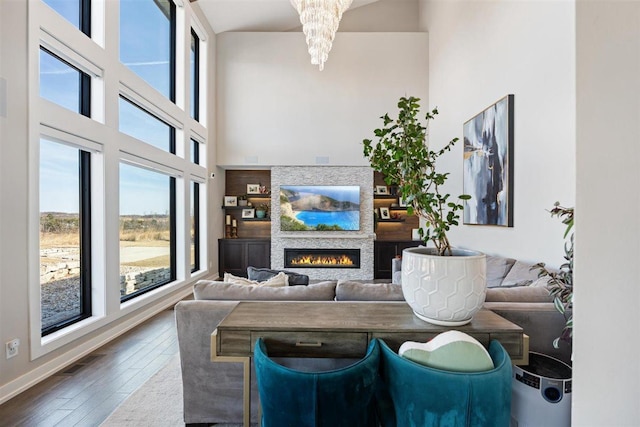 living room featuring hardwood / wood-style floors, baseboards, visible vents, a high ceiling, and a warm lit fireplace