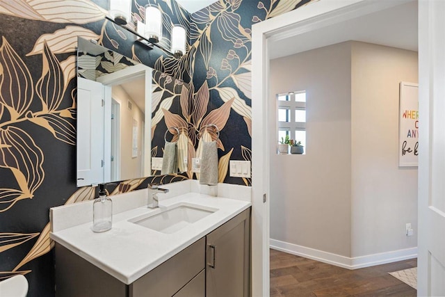 bathroom featuring wallpapered walls, vanity, baseboards, and wood finished floors