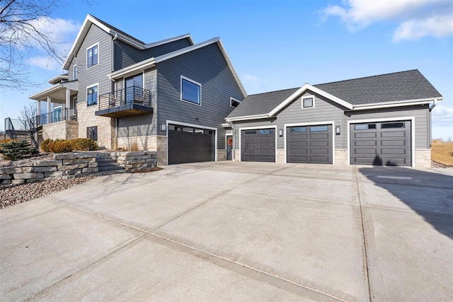 view of home's exterior with stone siding, a balcony, driveway, and a garage