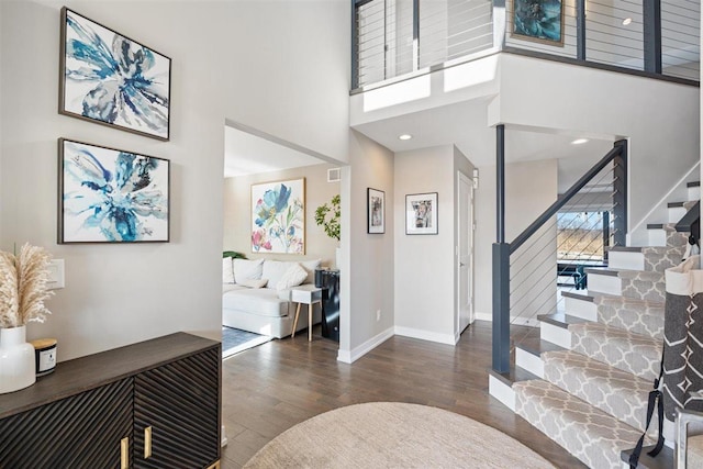 foyer featuring baseboards, stairs, recessed lighting, a towering ceiling, and wood finished floors