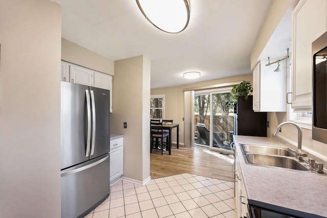 kitchen with a sink, freestanding refrigerator, white cabinets, light countertops, and light tile patterned floors