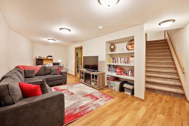 living room with light wood-style flooring, built in shelves, and stairs