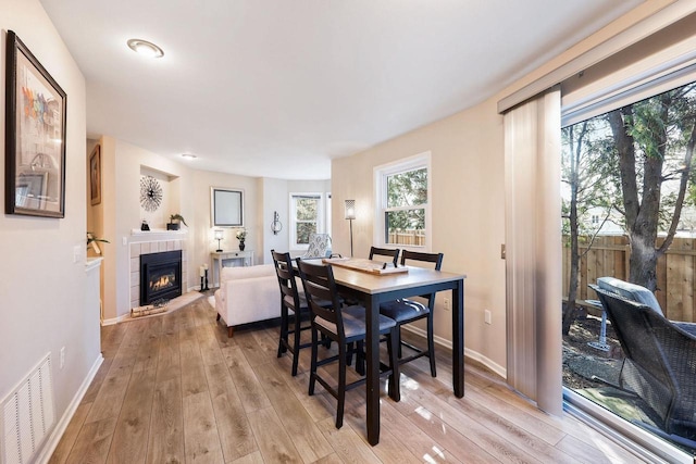 dining space with light wood-type flooring, visible vents, baseboards, and a tile fireplace