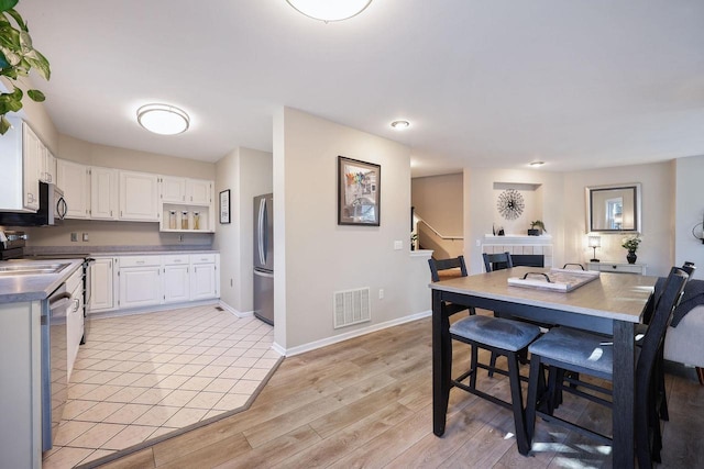 dining area featuring visible vents, light wood-style flooring, stairway, and baseboards