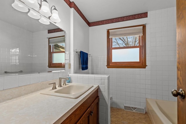 bathroom with tile patterned flooring, visible vents, a tub, vanity, and tile walls