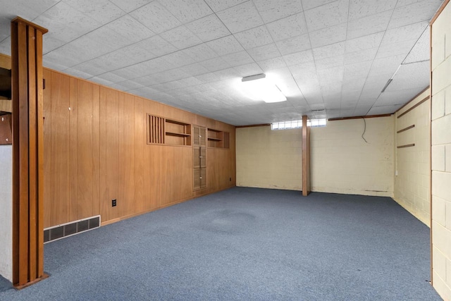 below grade area featuring visible vents, carpet flooring, concrete block wall, and wooden walls