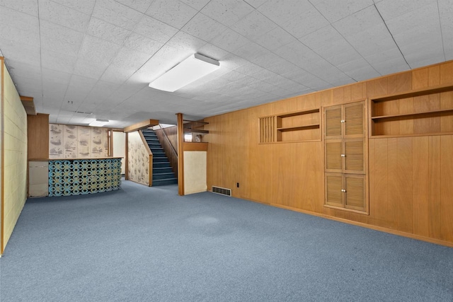 finished basement with carpet flooring, wooden walls, visible vents, and stairs