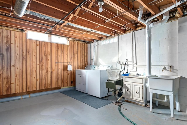 below grade area featuring a sink, wooden walls, washing machine and dryer, and concrete block wall