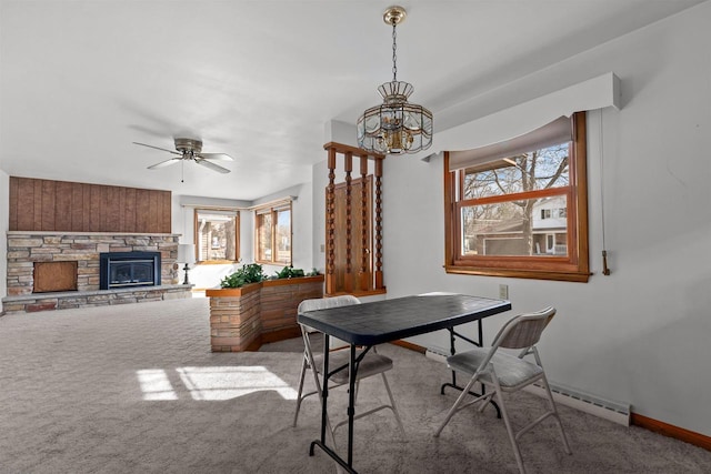 carpeted office with a stone fireplace, ceiling fan with notable chandelier, baseboards, and a wealth of natural light