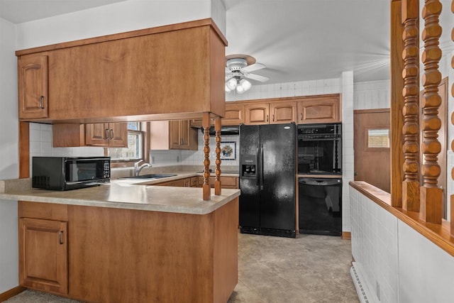 kitchen featuring brown cabinetry, a peninsula, black appliances, and a sink