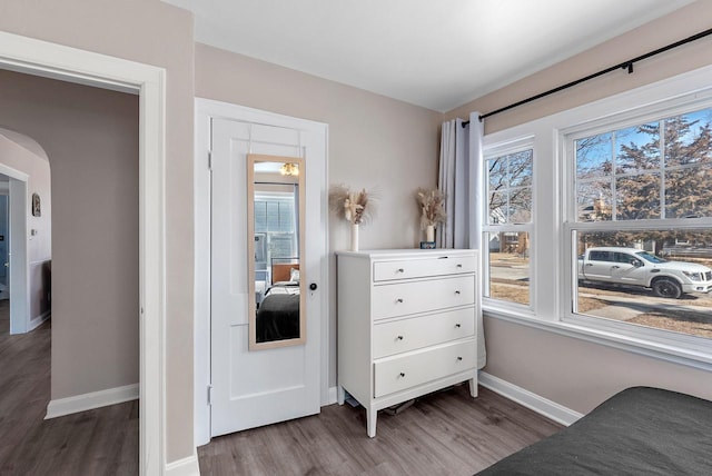 bedroom with baseboards, arched walkways, and wood finished floors