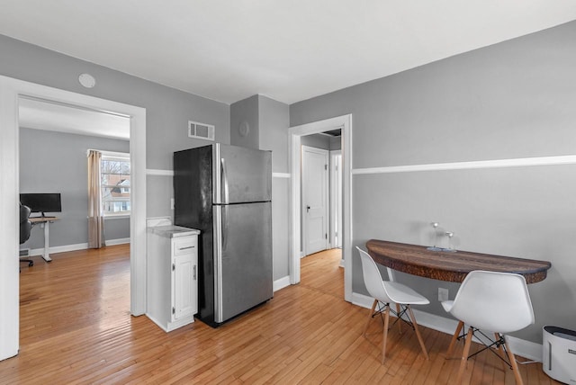 kitchen with light wood finished floors, visible vents, baseboards, freestanding refrigerator, and white cabinetry