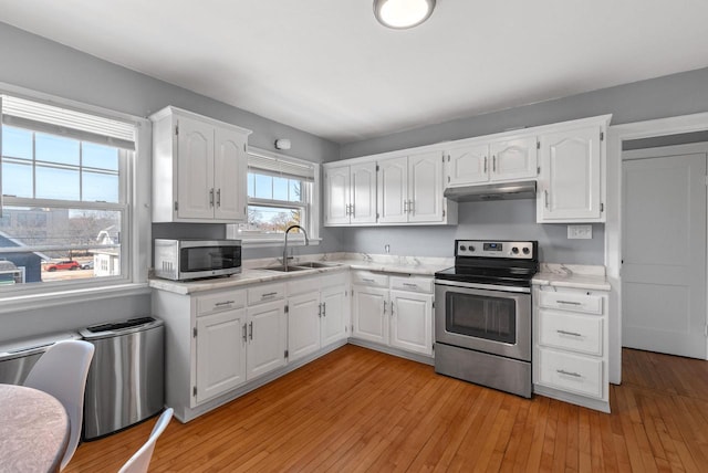 kitchen with under cabinet range hood, white cabinets, light wood-style flooring, and appliances with stainless steel finishes