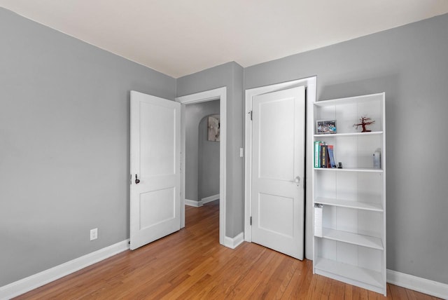 unfurnished bedroom featuring wood finished floors, baseboards, and arched walkways