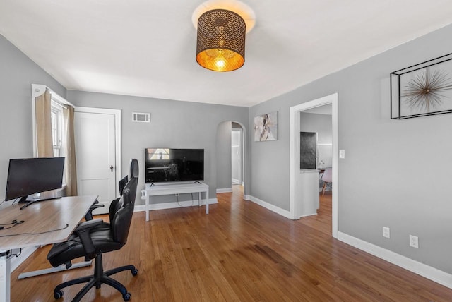 office space featuring arched walkways, visible vents, baseboards, and wood finished floors