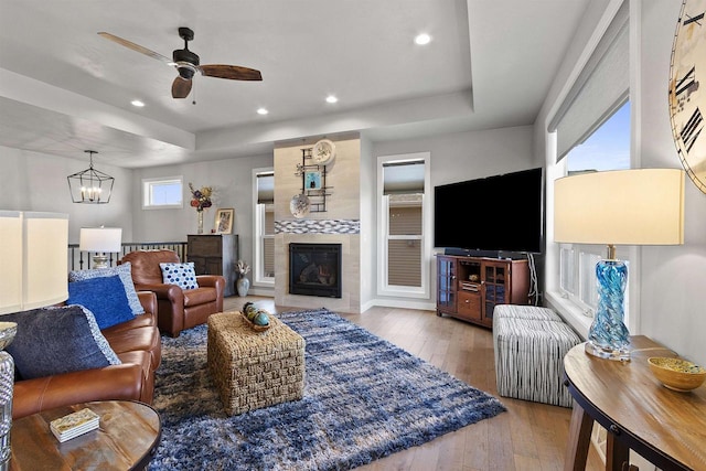 living area with a tiled fireplace, a tray ceiling, hardwood / wood-style flooring, and recessed lighting