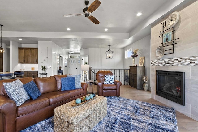 living area with recessed lighting, ceiling fan with notable chandelier, a fireplace, and light wood-type flooring