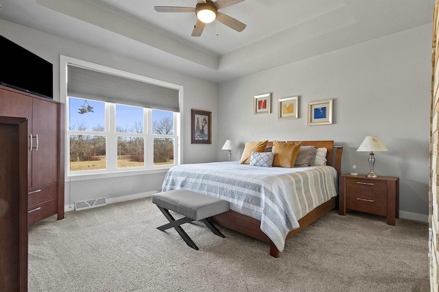 bedroom featuring light carpet, visible vents, baseboards, and a tray ceiling